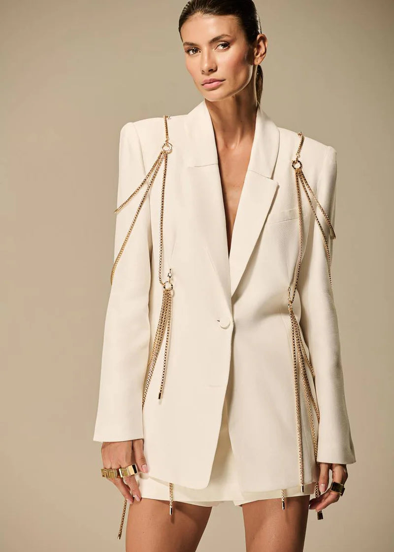 Woman wearing a cream blazer dress with gold chain details on a beige background