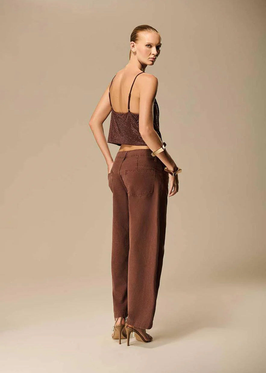 Woman wearing a brown top and pants against a beige background