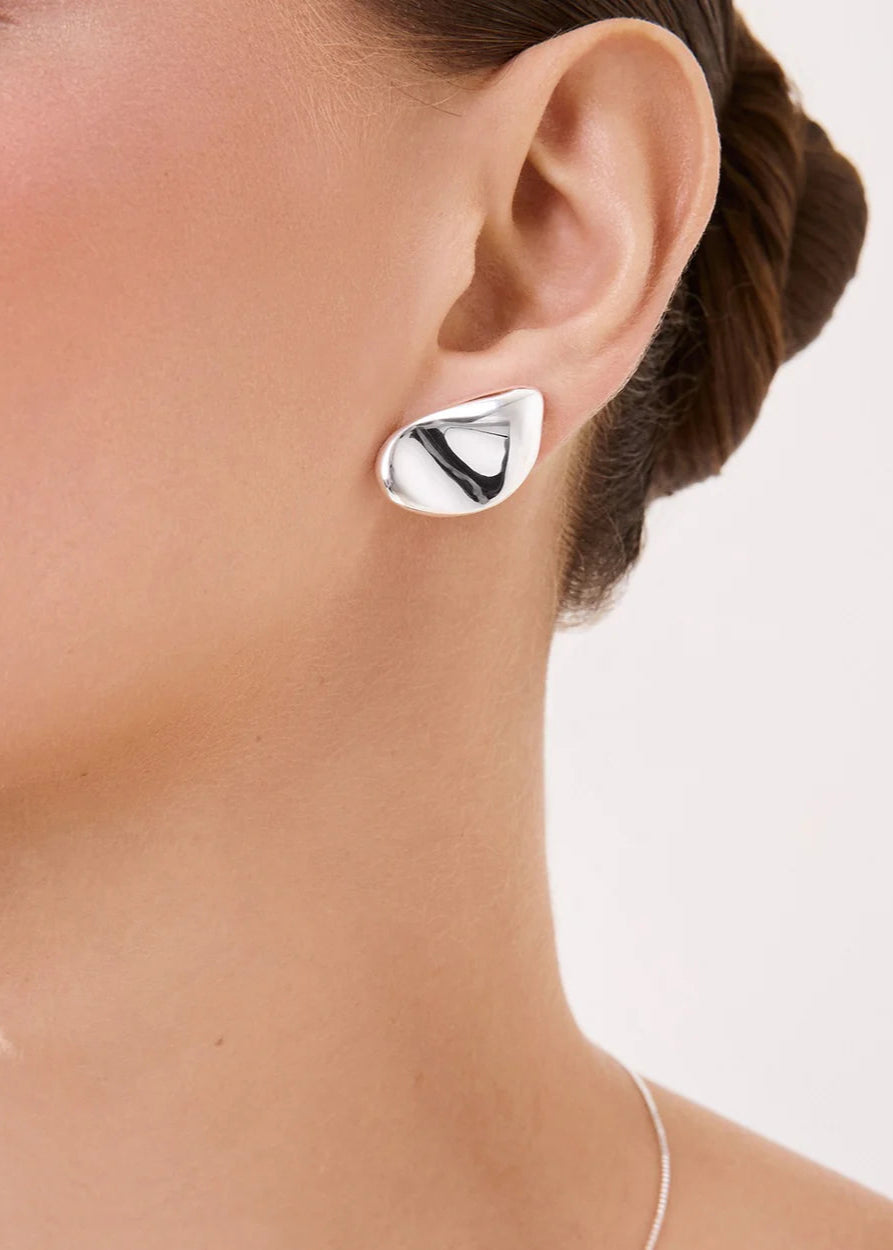 Silver earring worn by a person on a white background