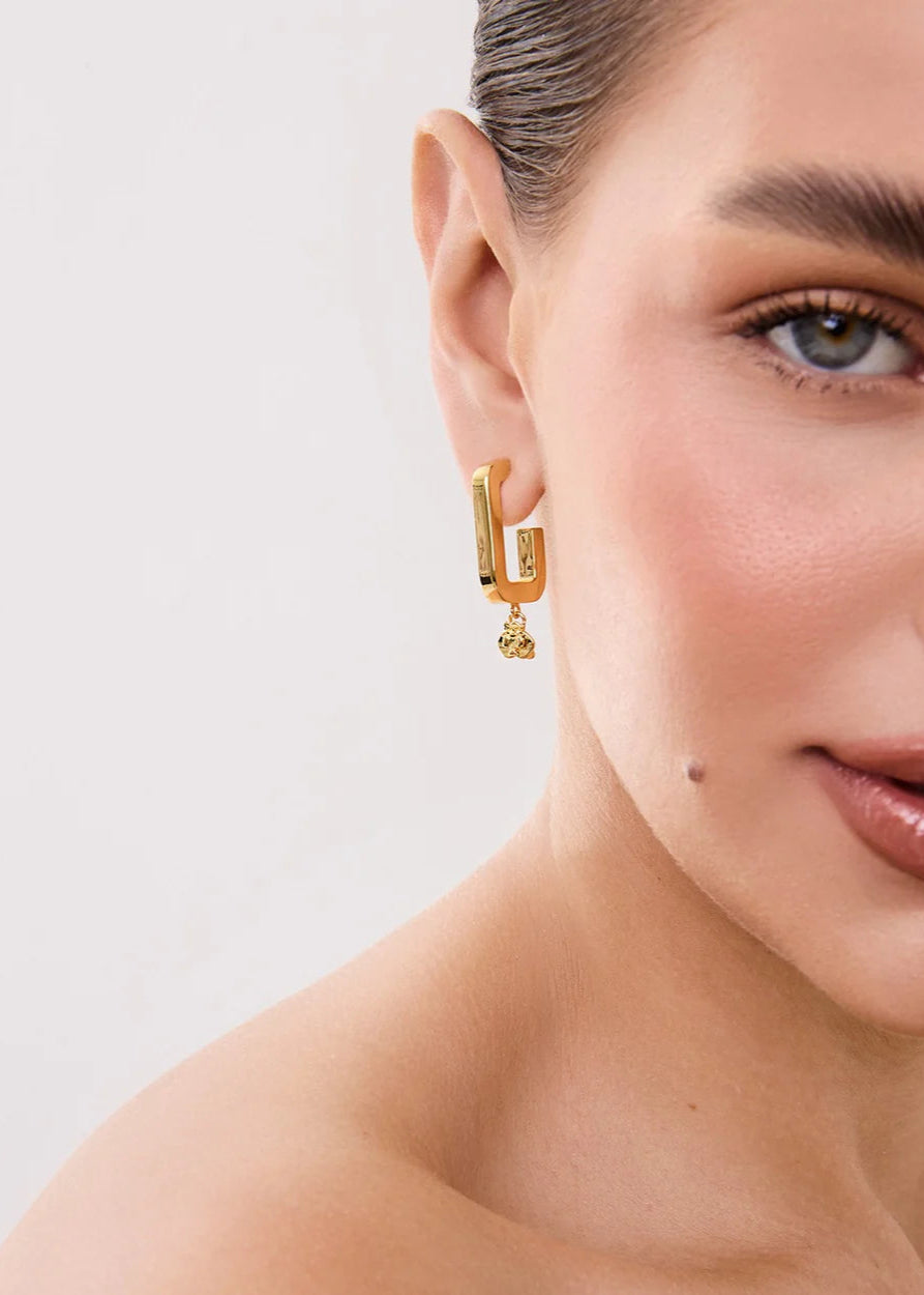 Close-up of a person wearing gold hoop earrings with a neutral background