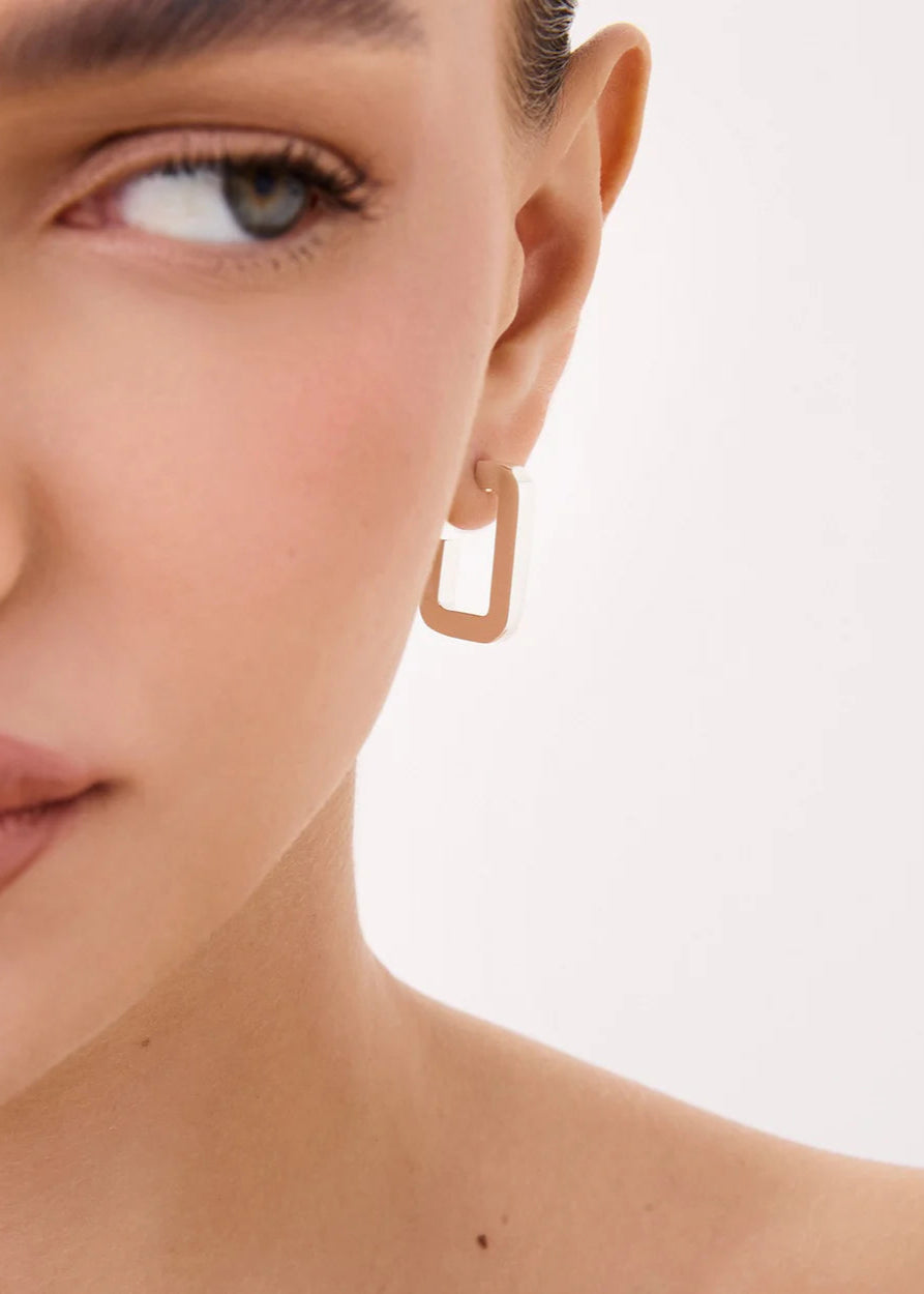 Close-up of a person wearing a gold hoop earring on a neutral background