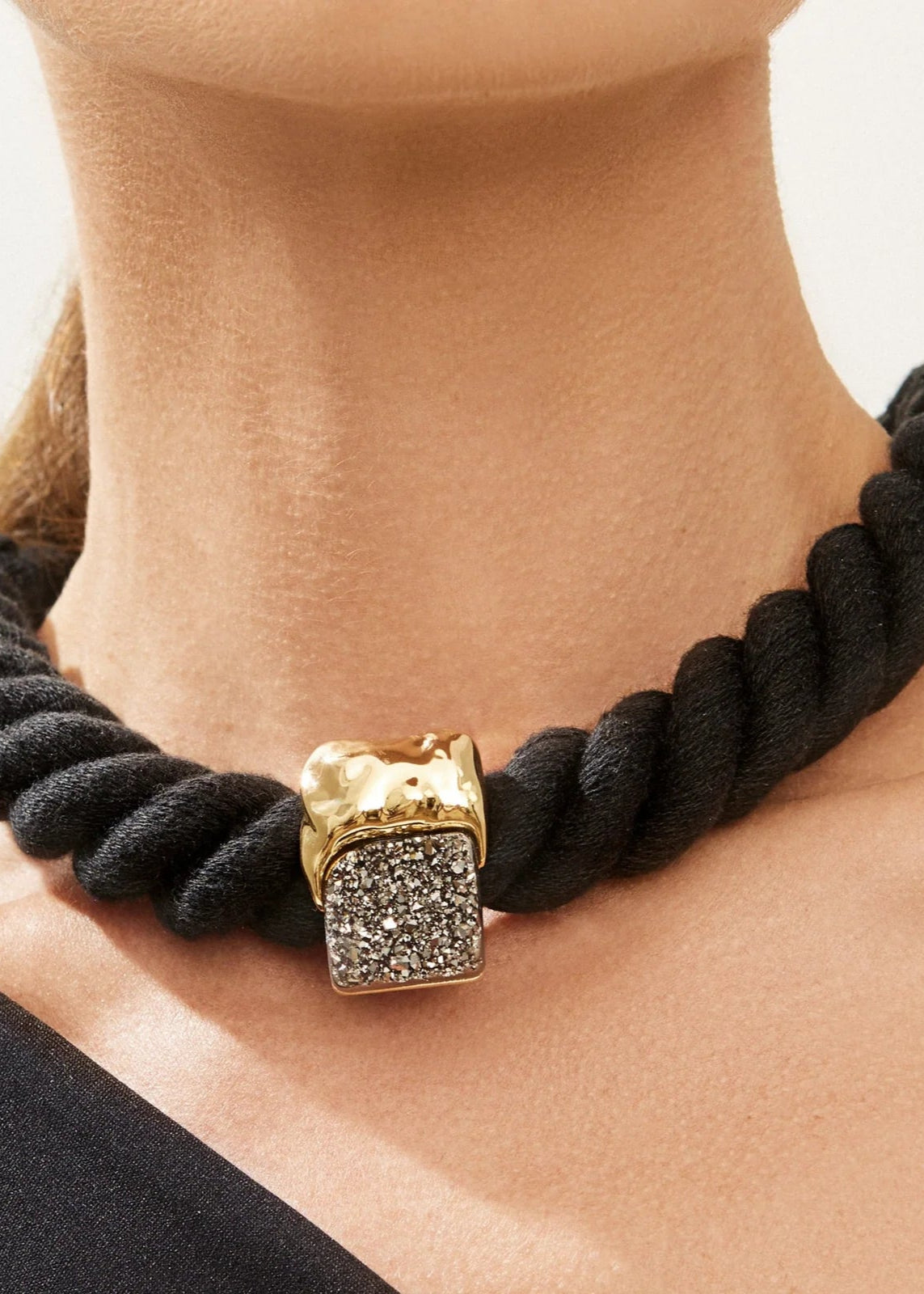 Black rope-style necklace with a gold clasp worn by a person