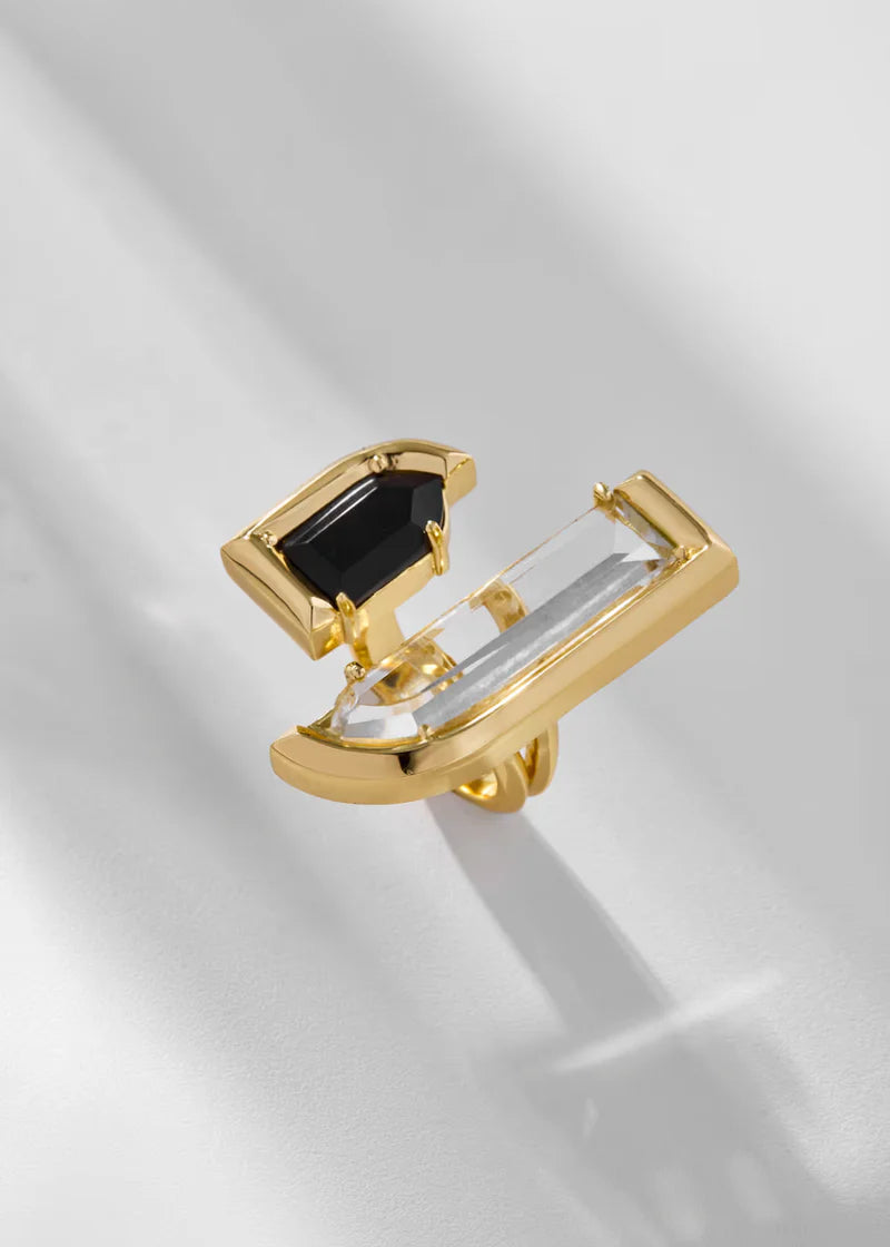 Gold ring with black and clear gemstones on a light gray background