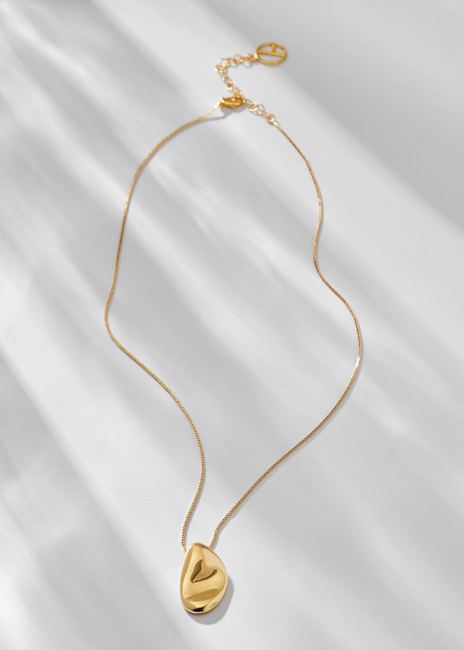 Gold necklace with a teardrop-shaped pendant on a white fabric background