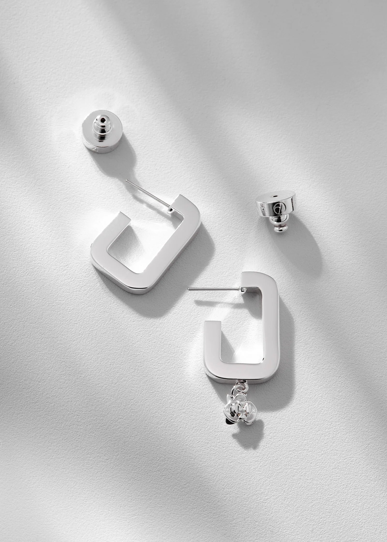Pair of silver hoop earrings with a central gemstone on a light gray background