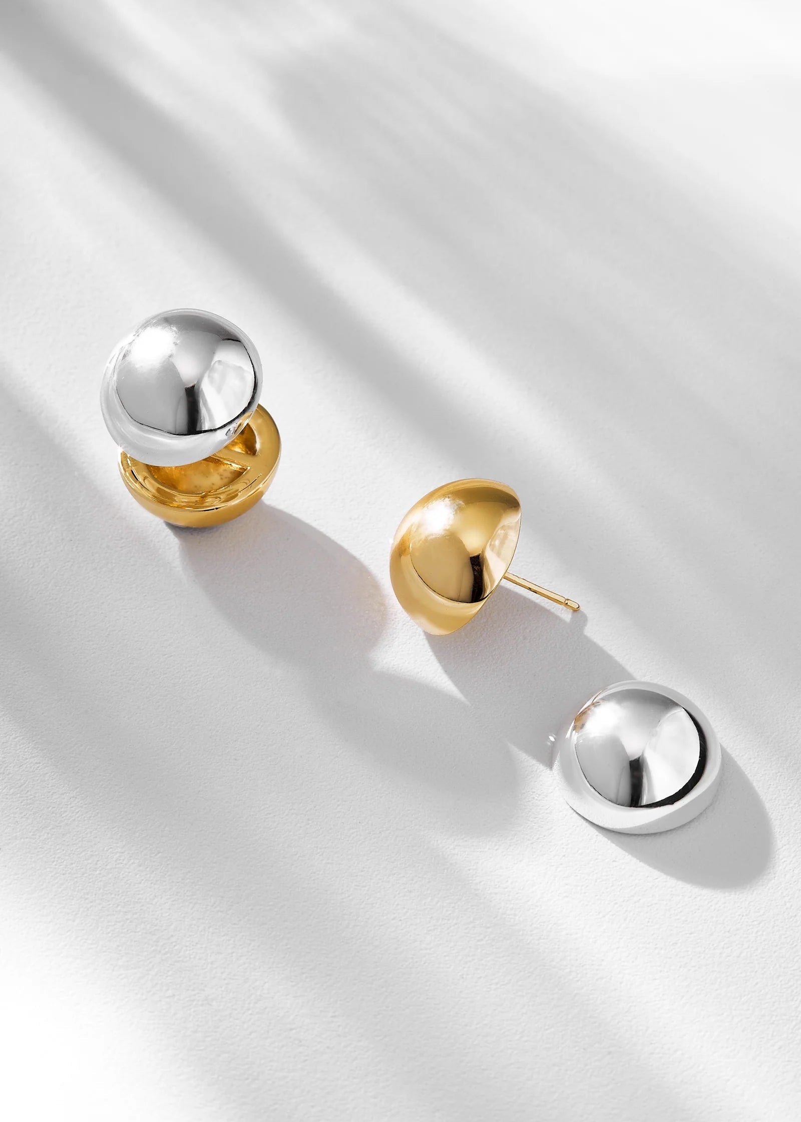 Pair of gold and silver spherical earrings on a light gray background