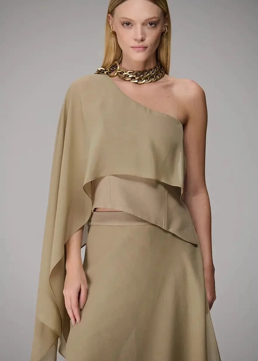 Woman wearing a beige one-shoulder dress with a gold necklace on a gray background