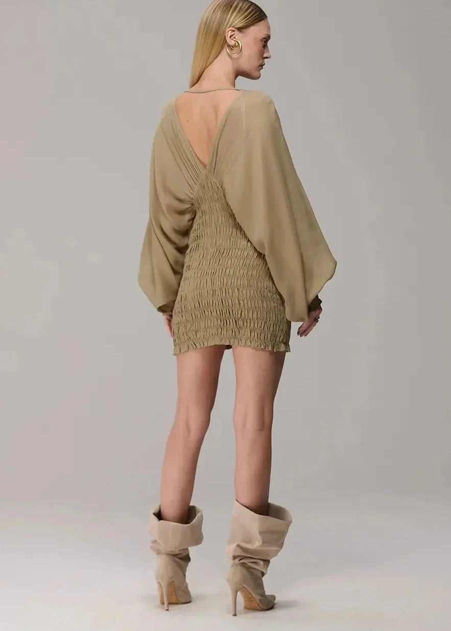 Woman wearing a beige dress with a backless design and matching high-heeled boots on a plain background