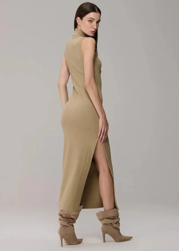 Woman wearing a beige sleeveless dress with a slit and matching boots on a plain background