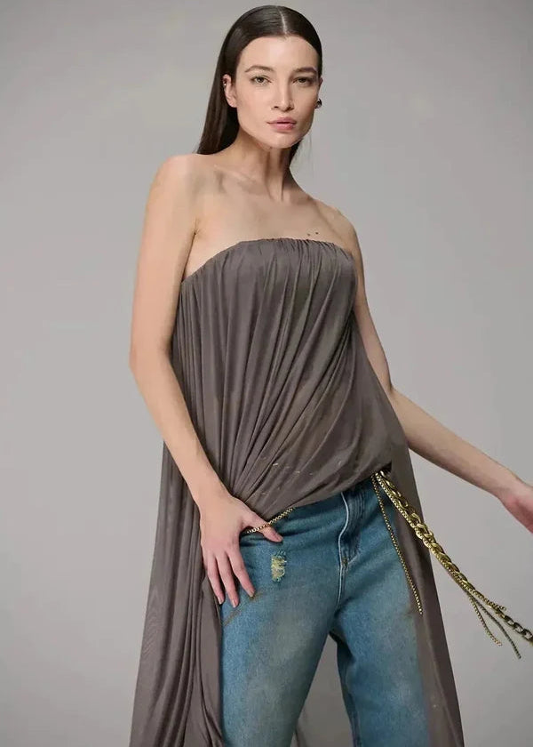 Woman wearing a strapless army top and blue jeans with a gold chain, on a plain background