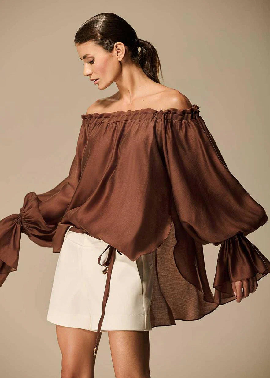 Woman wearing a brown off-shoulder blouse and white shorts against a beige background