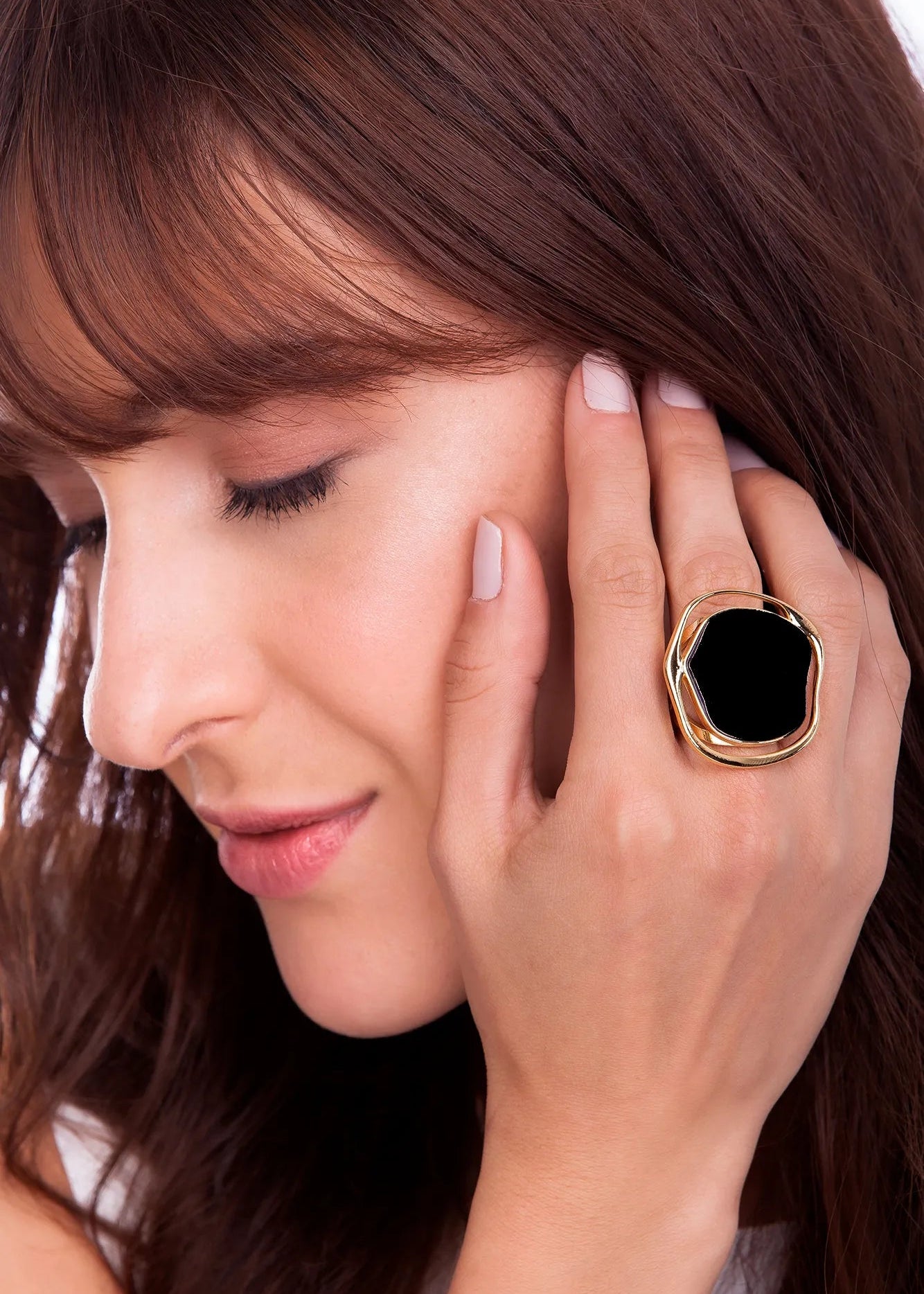 Woman wearing a large ring with a black gemstone, touching her face.