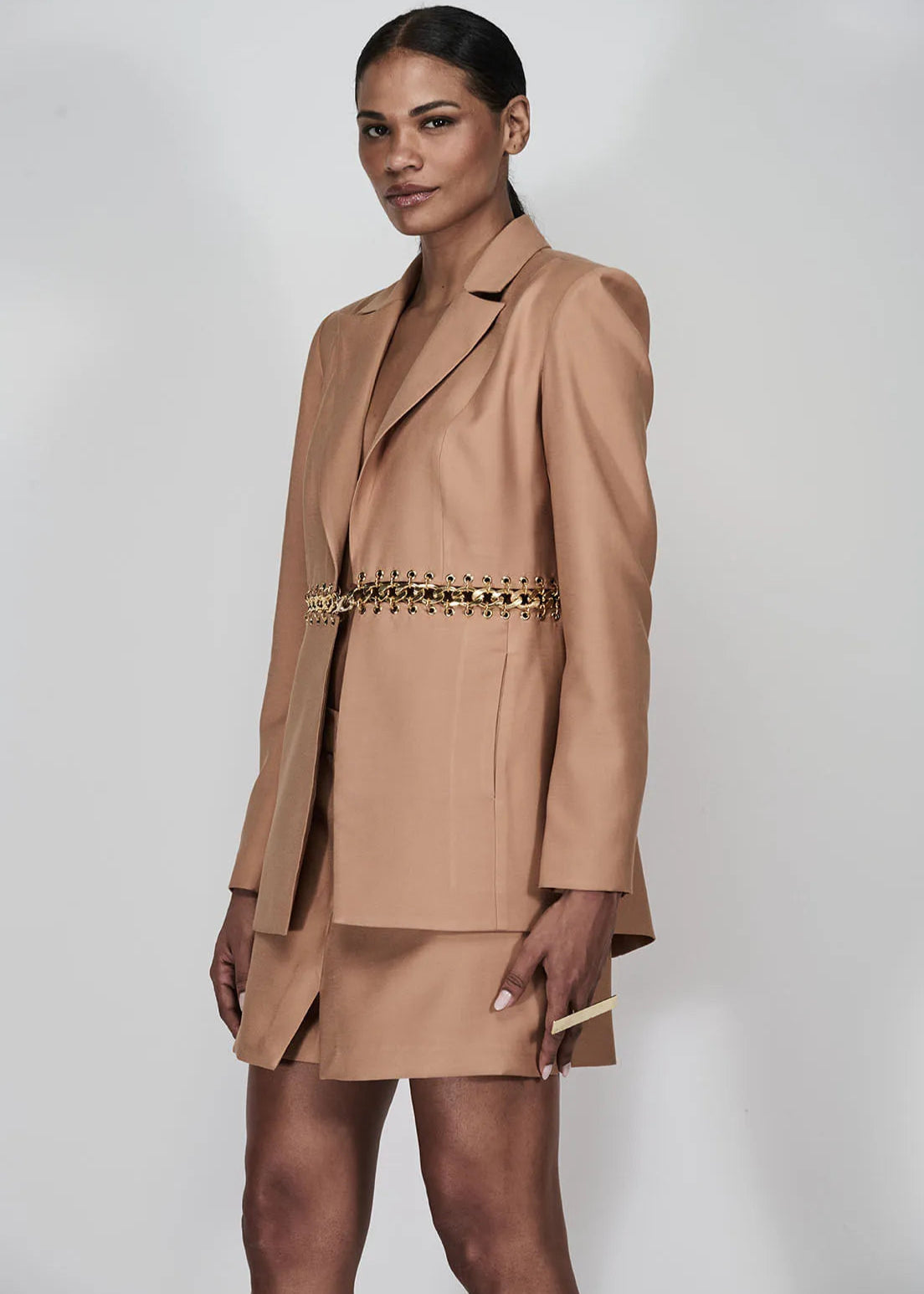 Woman wearing a beige suit with a gold belt on a white background