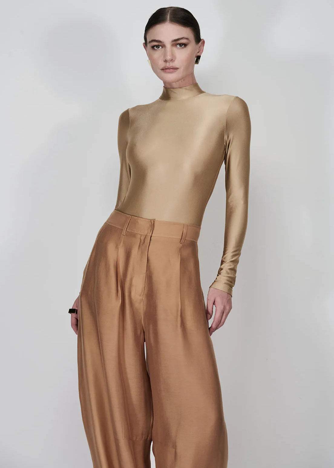 Person wearing a gold long-sleeve top and brown wide-leg pants on a white background