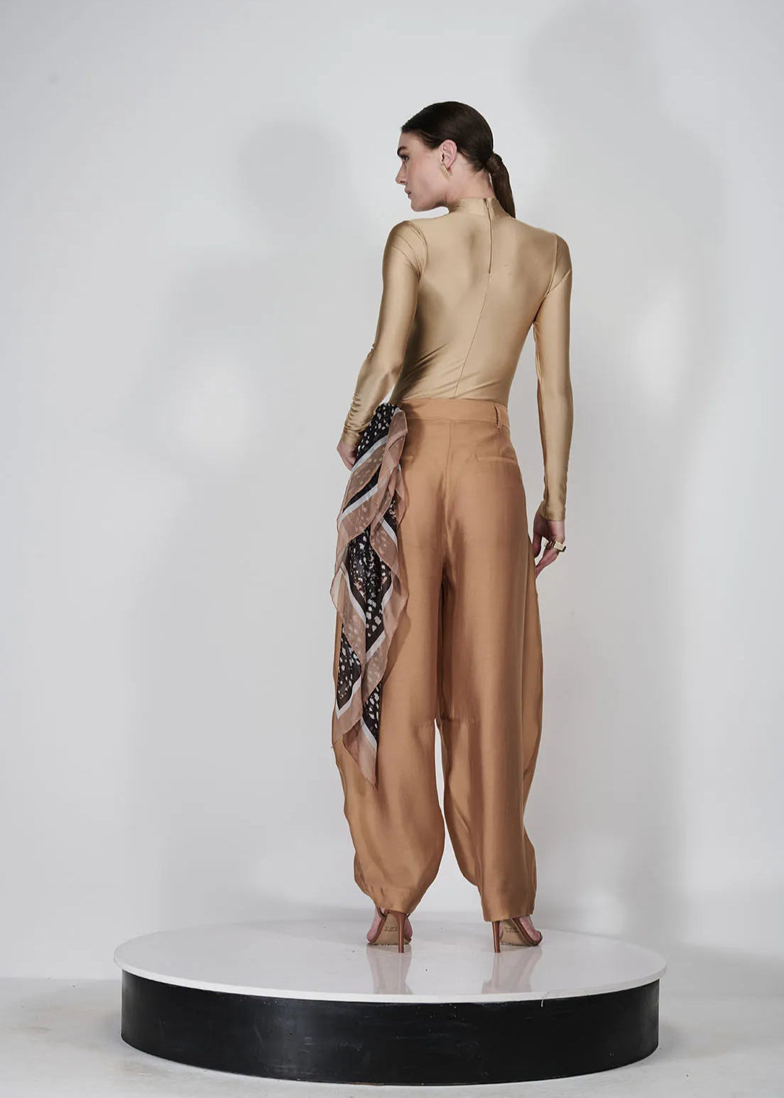 Woman wearing a gold top and brown pants with a patterned scarf on a white background