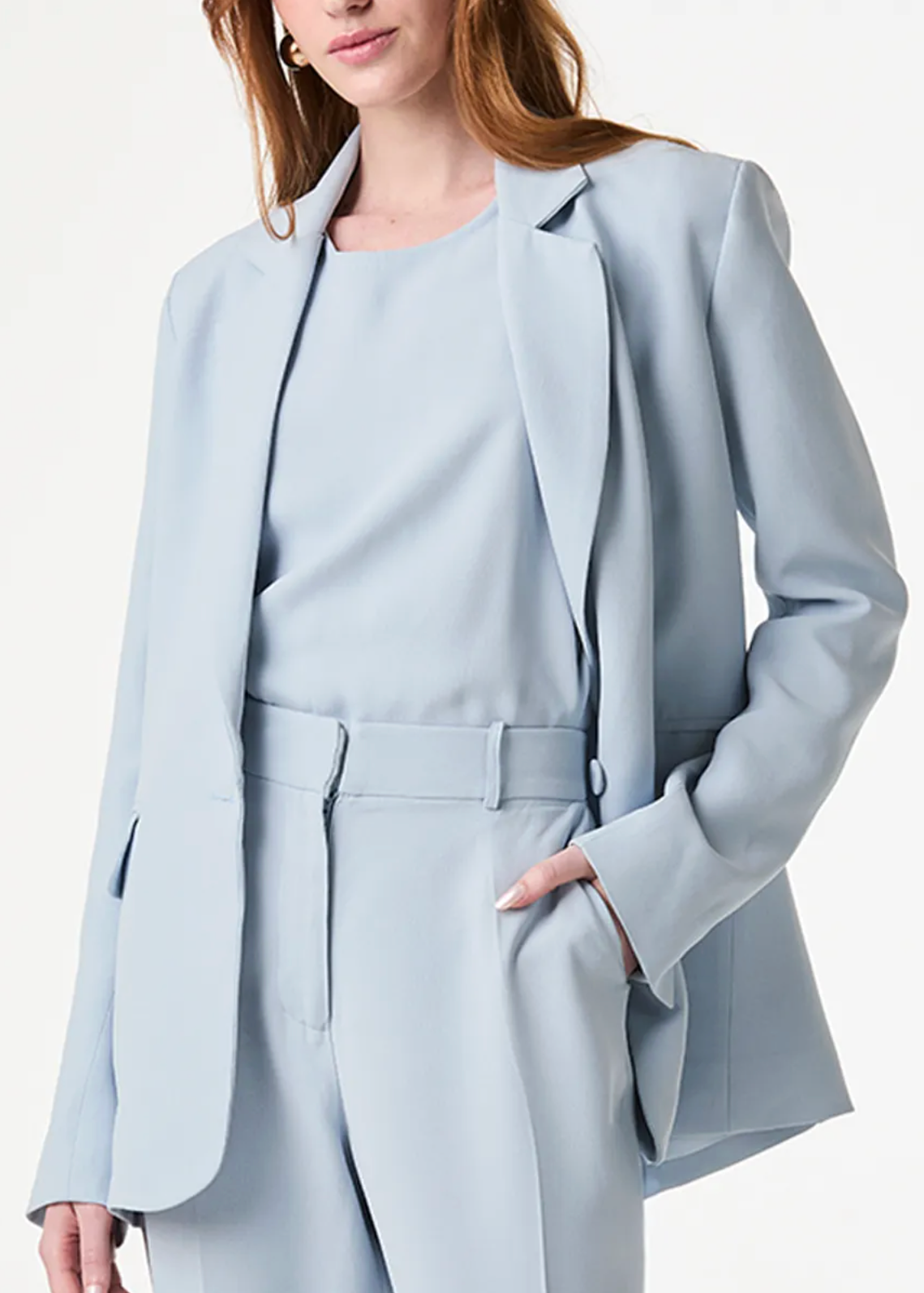 A woman wearing a light blue tailored suit with a blazer, matching top, and trousers against a clean white studio background.
