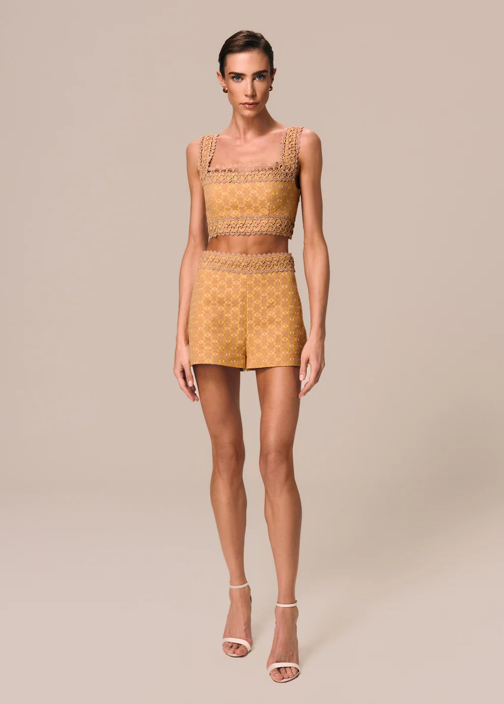 Woman wearing a mustard yellow outfit with a matching top and shorts on a beige background