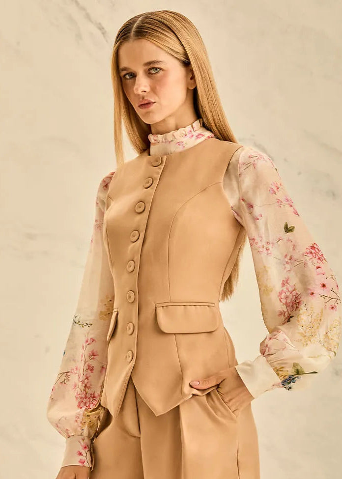 Woman wearing a beige vest and shorts set with a floral blouse against a neutral background