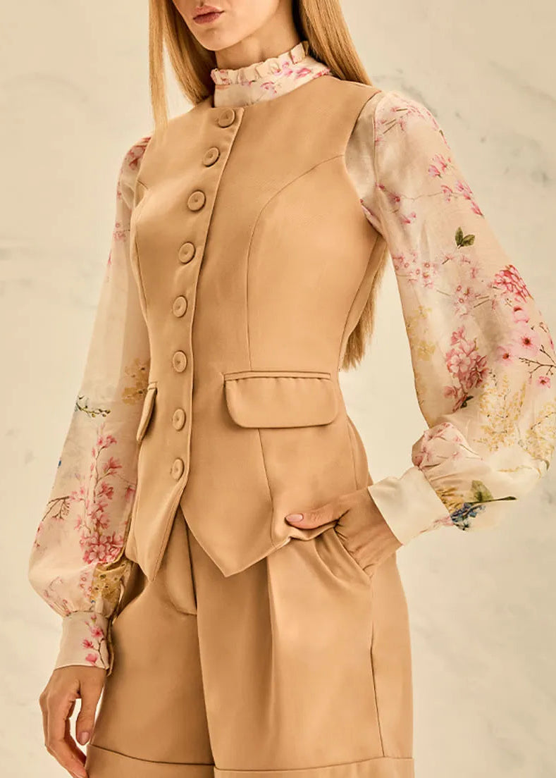 Woman wearing a beige vest with floral blouse against a neutral background
