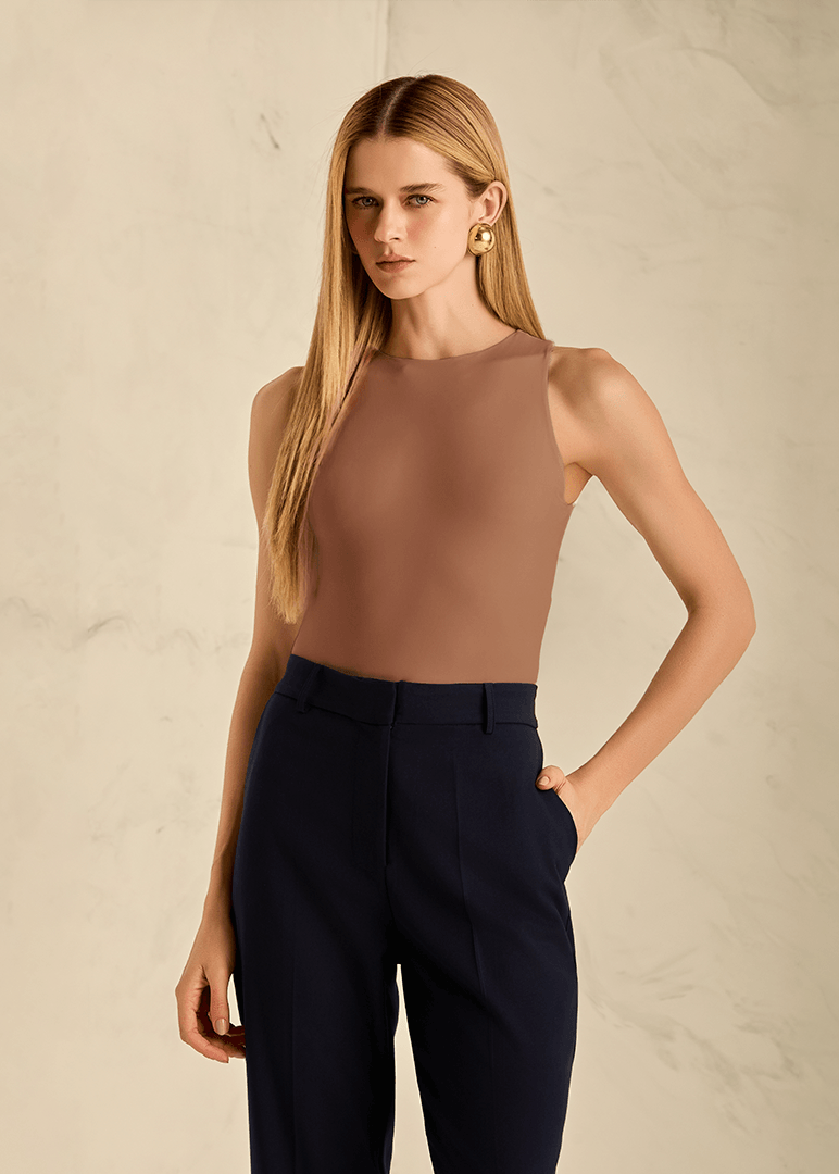 Woman wearing a brown sleeveless top and black pants against a beige background