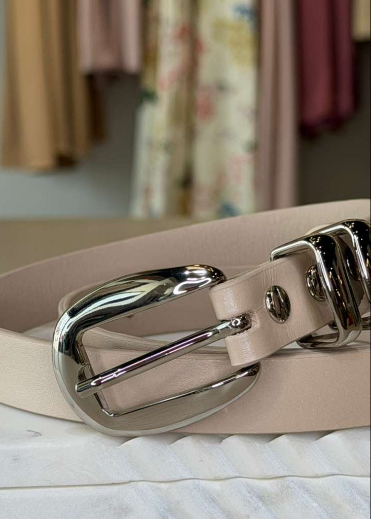 Beige leather belt with a silver buckle on a marble surface.
