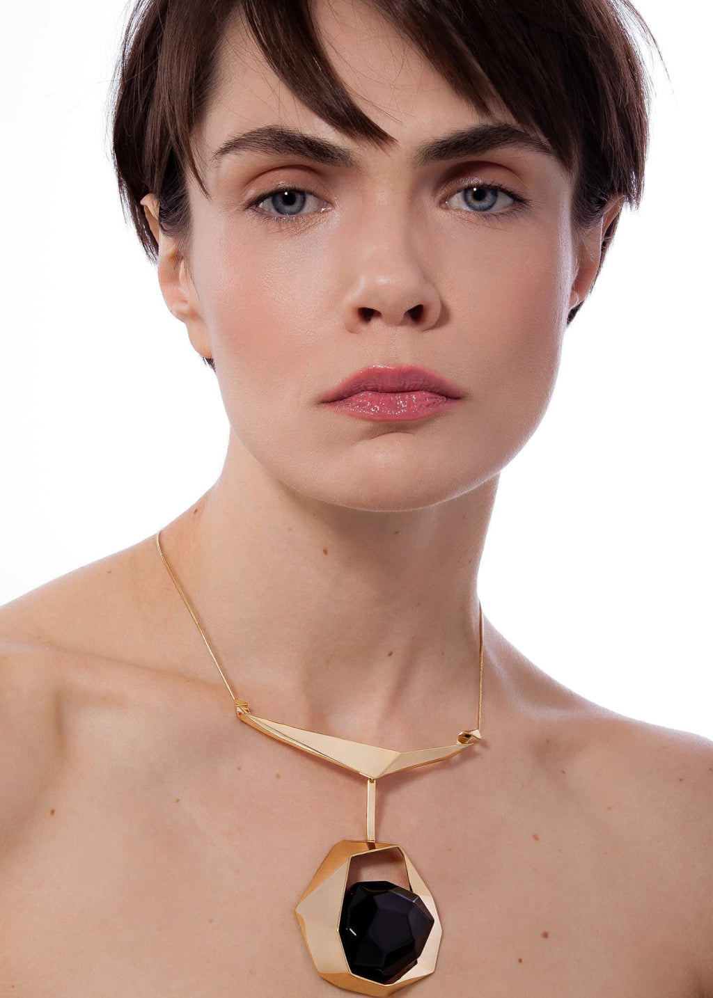Woman wearing a gold necklace with a black pendant on a white background