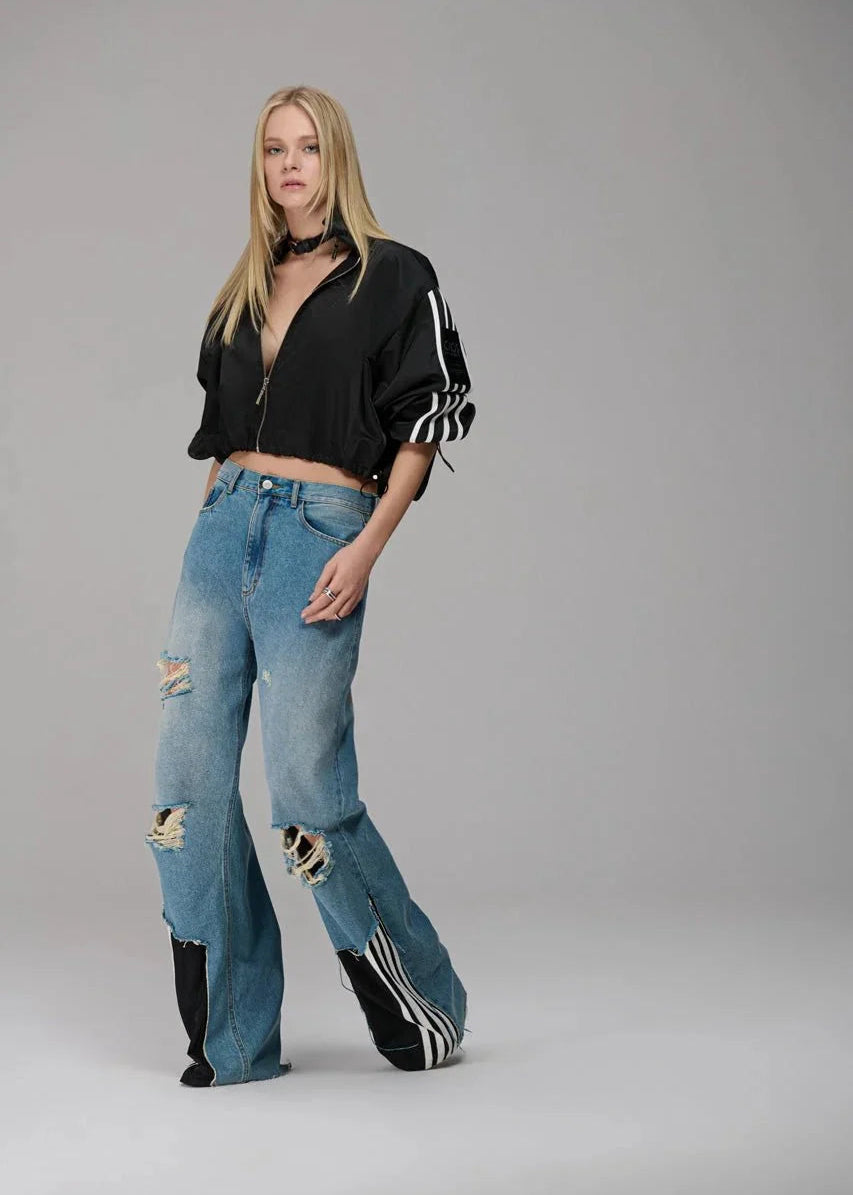 Woman wearing a black jacket, blue jeans, and black boots on a gray background