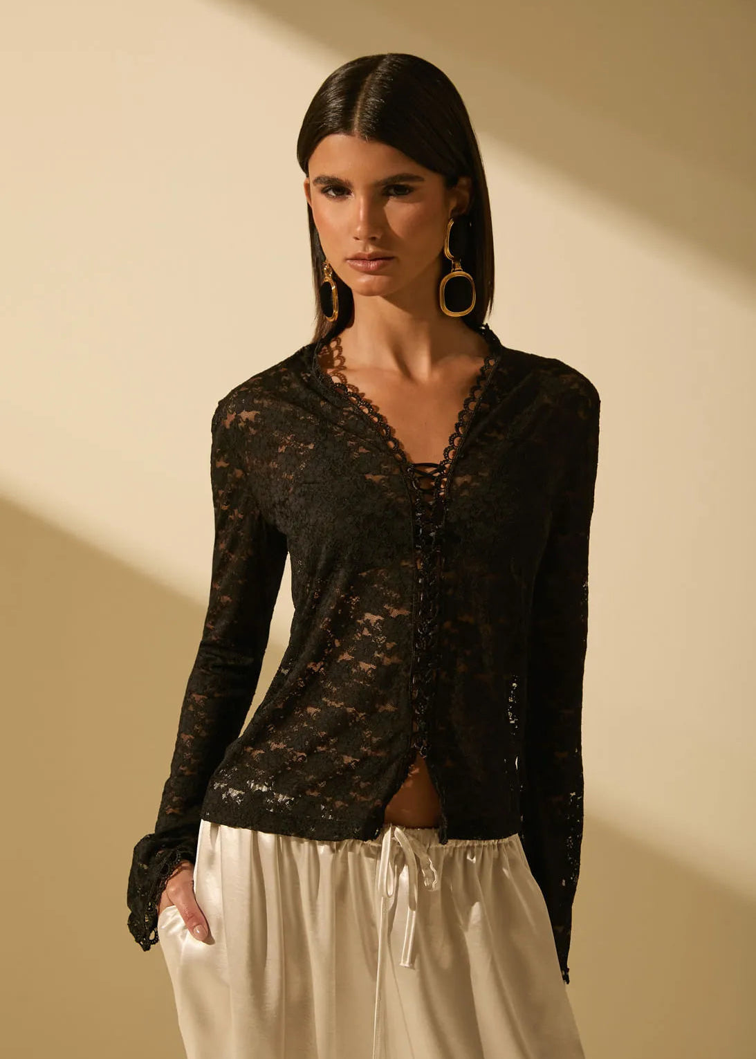 Woman wearing a black lace top and white pants against a beige background