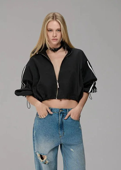 Woman wearing a black cropped jacket and blue jeans with rips on a gray background