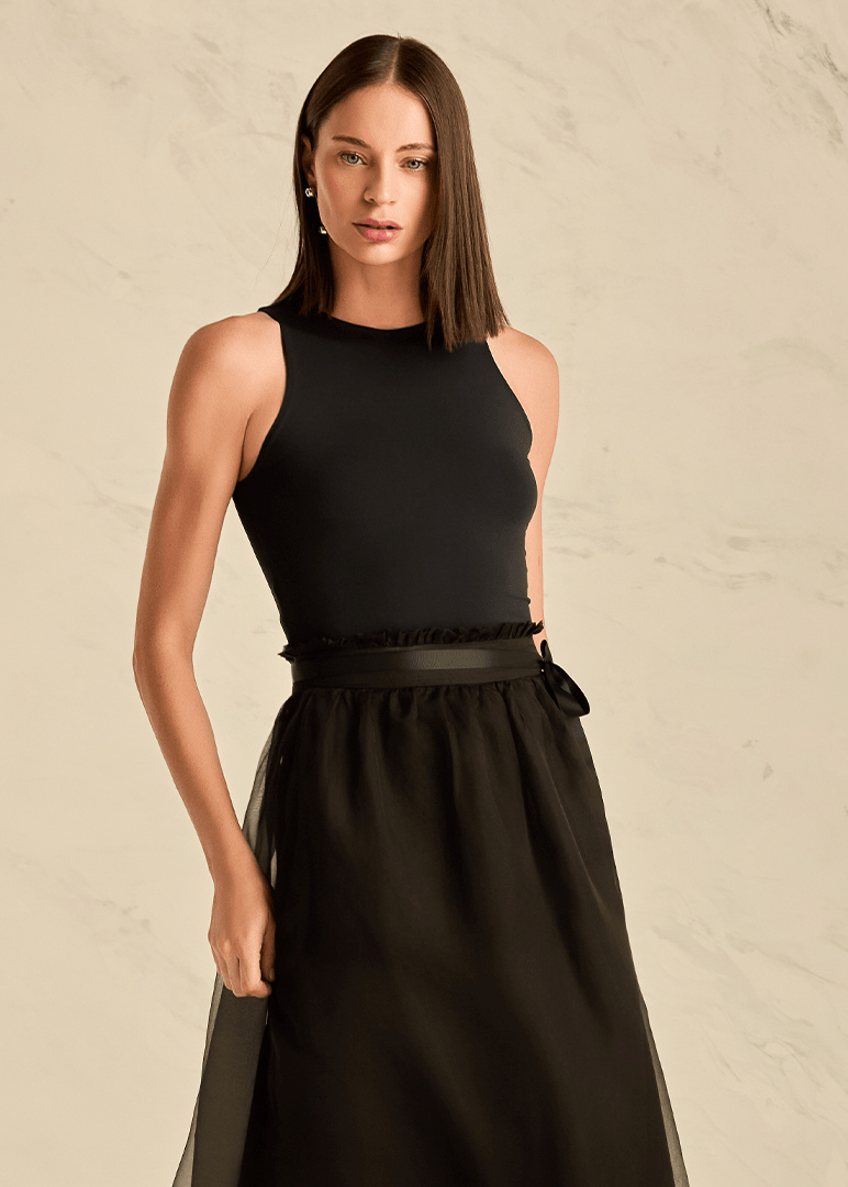 Woman wearing a black sleeveless top and skirt against a beige background