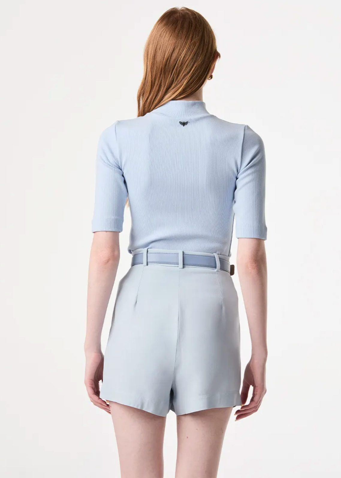 A woman shown from the back wearing a light blue ribbed short-sleeve polo-style top and matching light blue shorts against a plain white studio background.