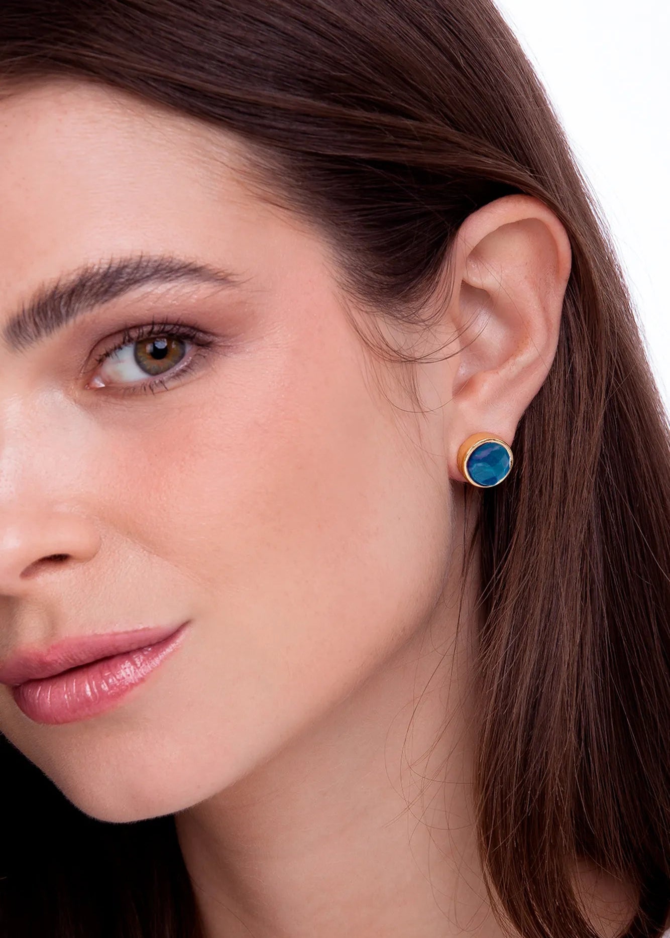 Close-up of a woman wearing a gold earring with a blue gemstone on a white background