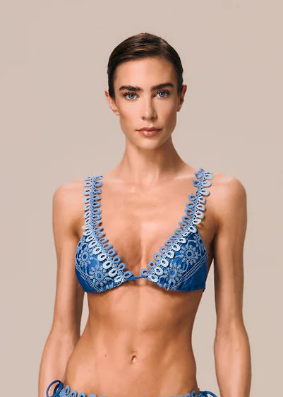 Woman wearing a blue bikini with intricate detailing on a beige background