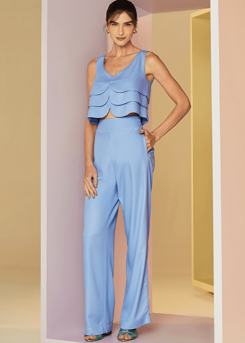 Woman wearing a light blue outfit with a ruffled top and wide-leg pants against a neutral background.