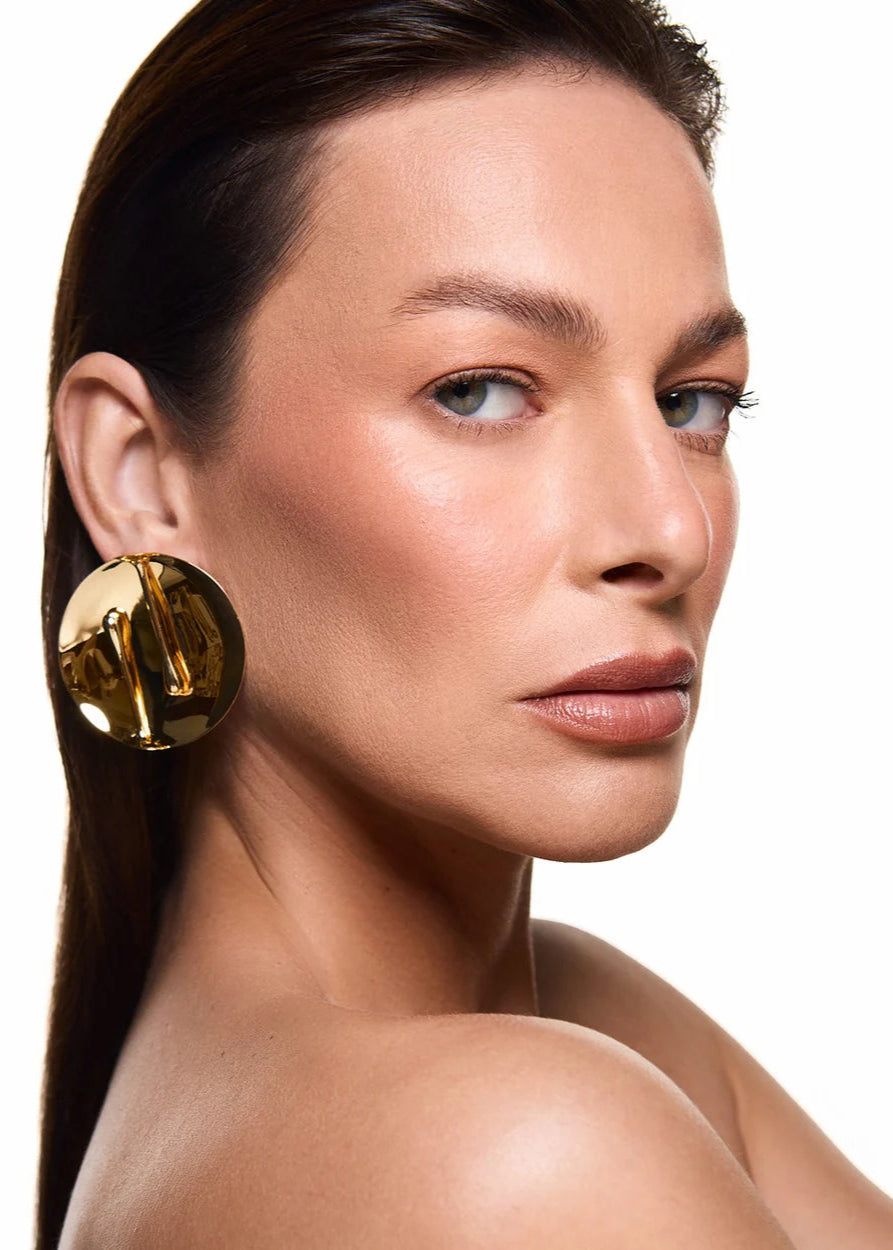 Woman wearing gold earrings with a neutral background