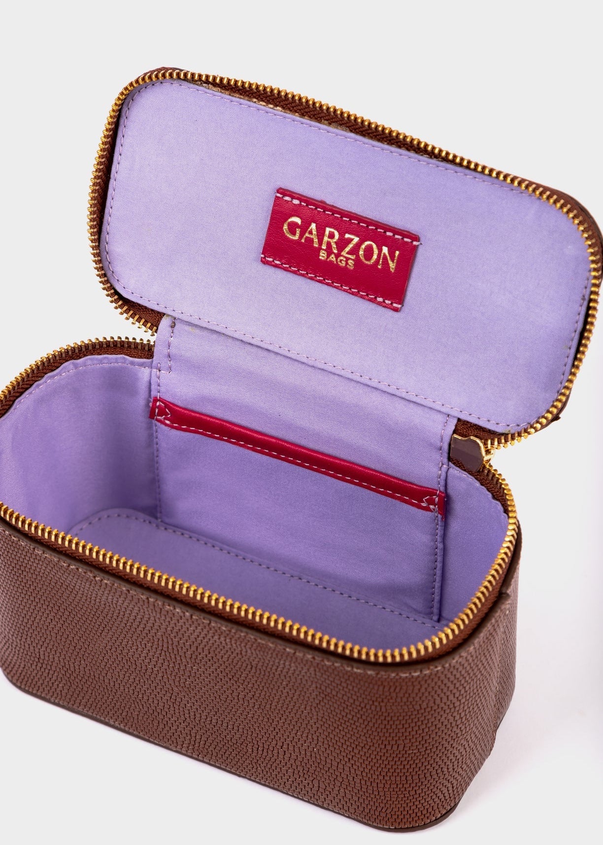 An open brown textured zippered case with a lavender purple interior, gold-tone zipper, and a red interior label reading GARZON BAGS.