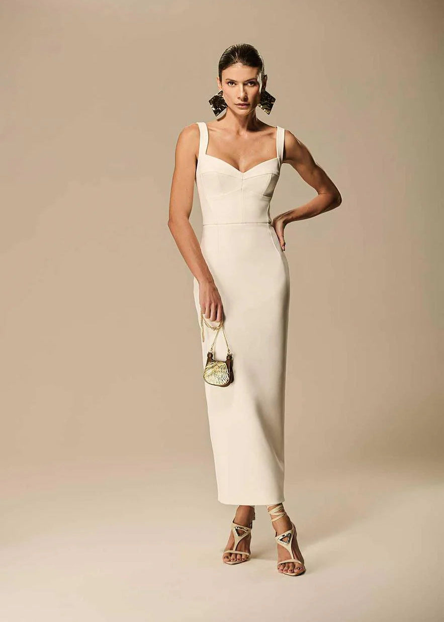 Woman in a white dress holding a green handbag against a beige background