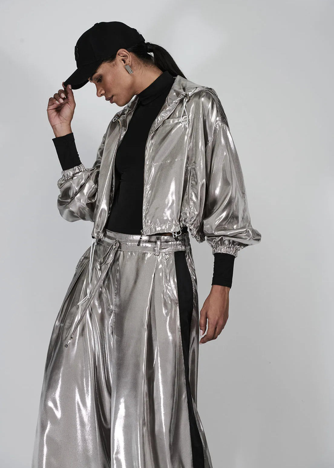 Person wearing a silver reflective outfit with a black cap on a plain background