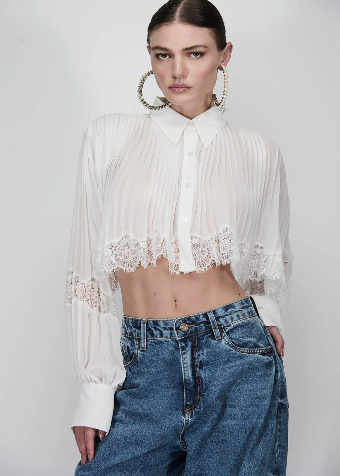 Person wearing a white lace top and blue jeans on a plain background