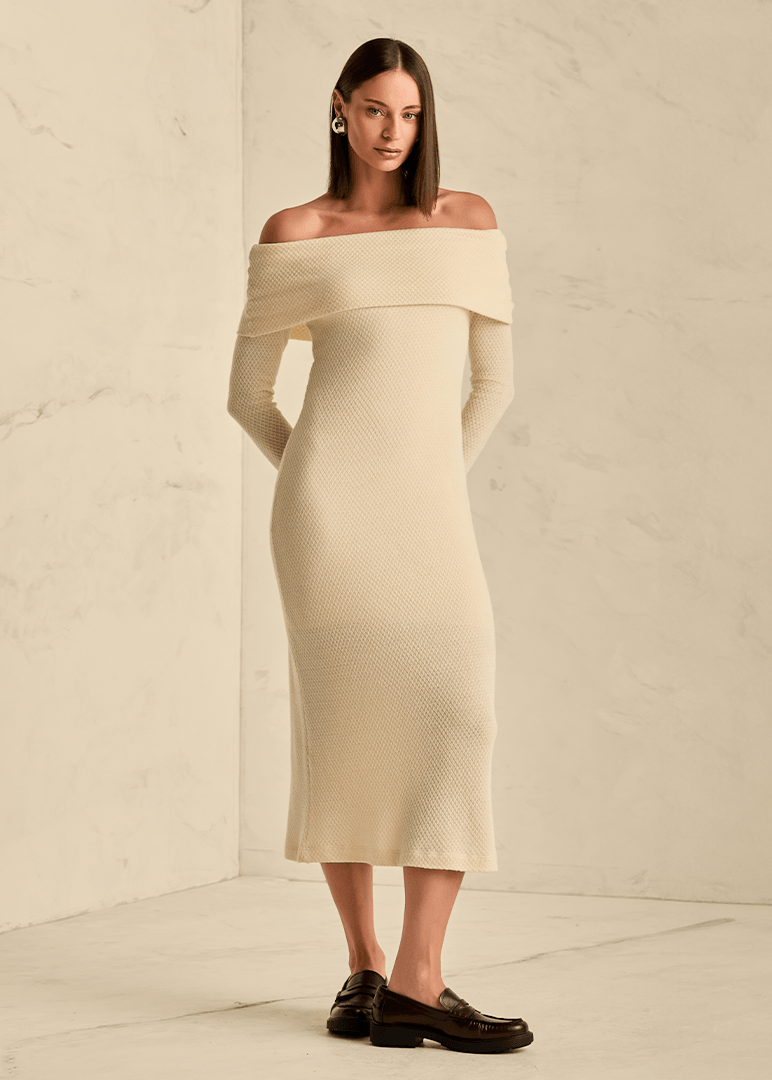 Woman wearing a beige off-shoulder dress against a plain background