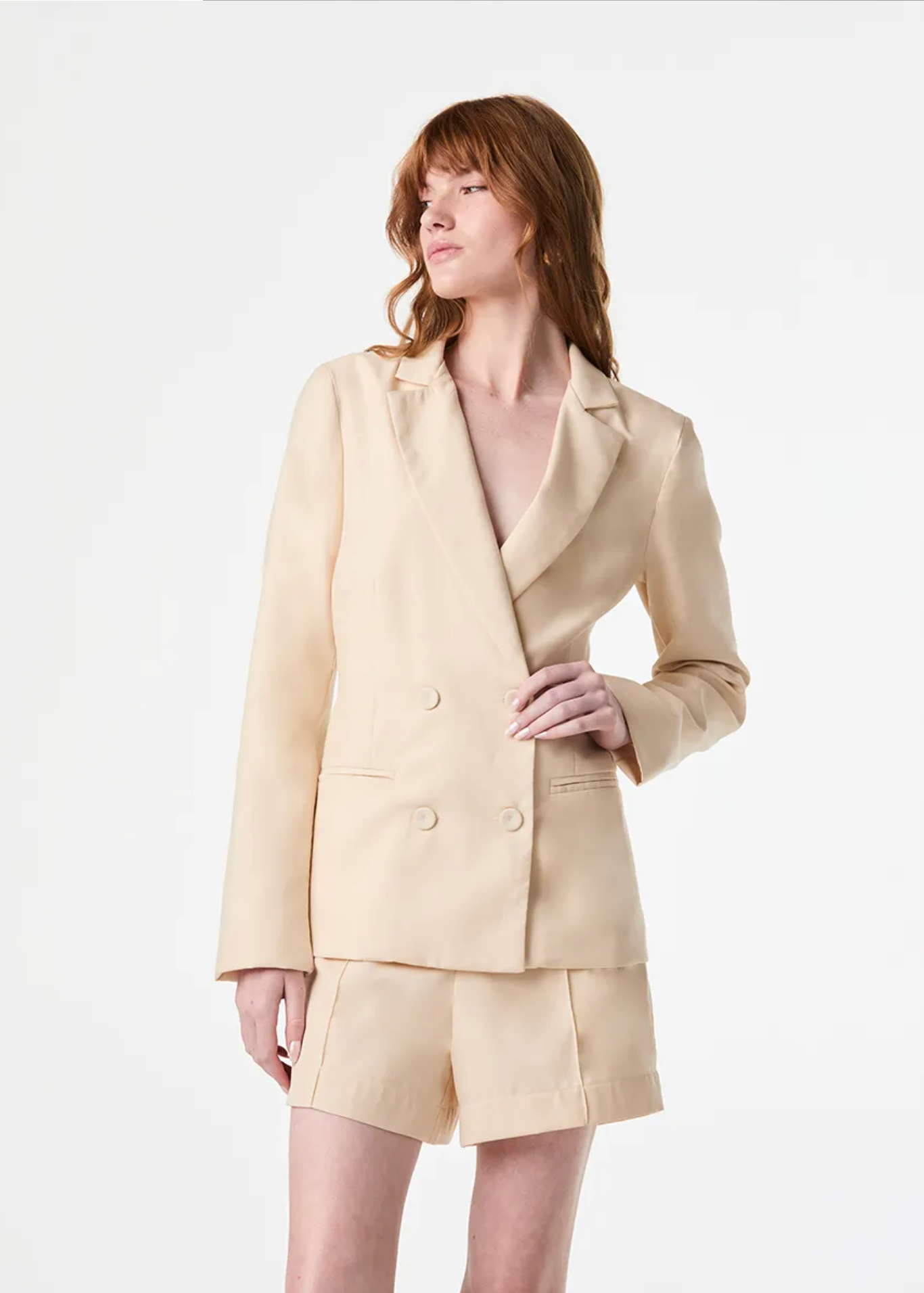 A model wearing a light beige double-breasted blazer and matching shorts set, photographed against a clean white studio background.