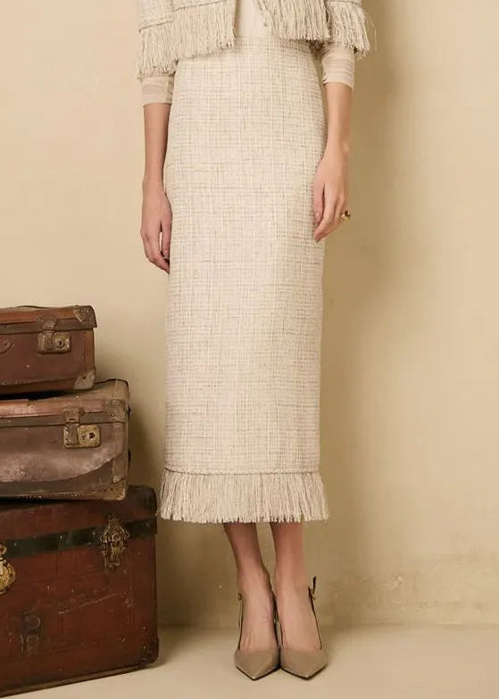 Woman in a tweed outfit tanding next to old suitcases against a beige background