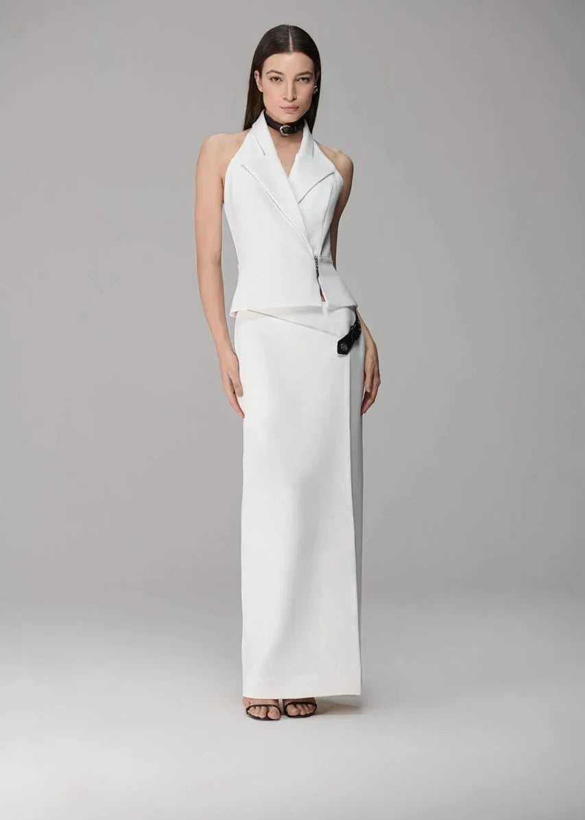 A model wearing a white sleeveless wrap-style maxi dress with structured shoulders and a draped waist, paired with a black choker and brown strappy sandals, set against a plain light gray studio background.