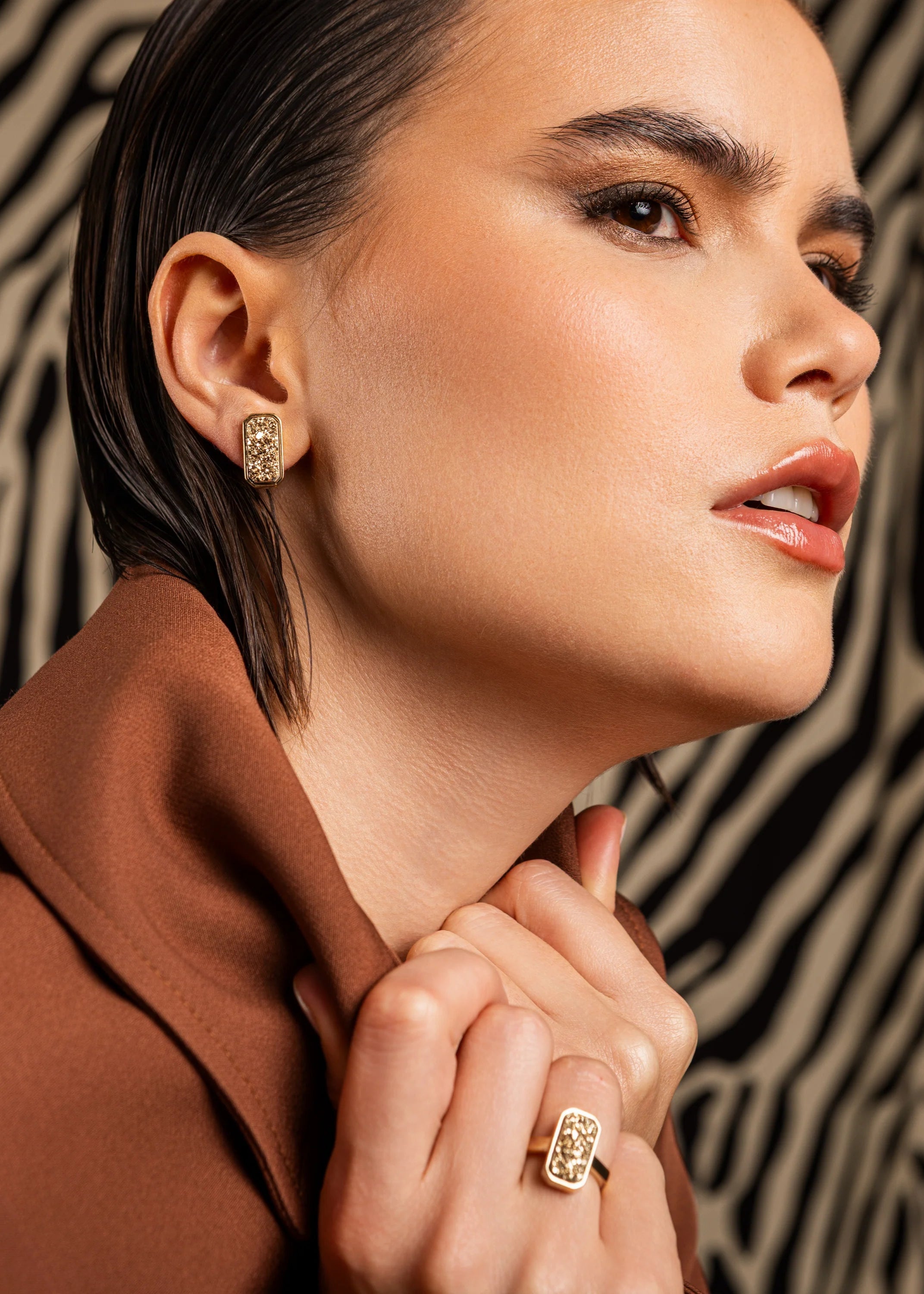 Woman wearing gold earrings and ring against a patterned background