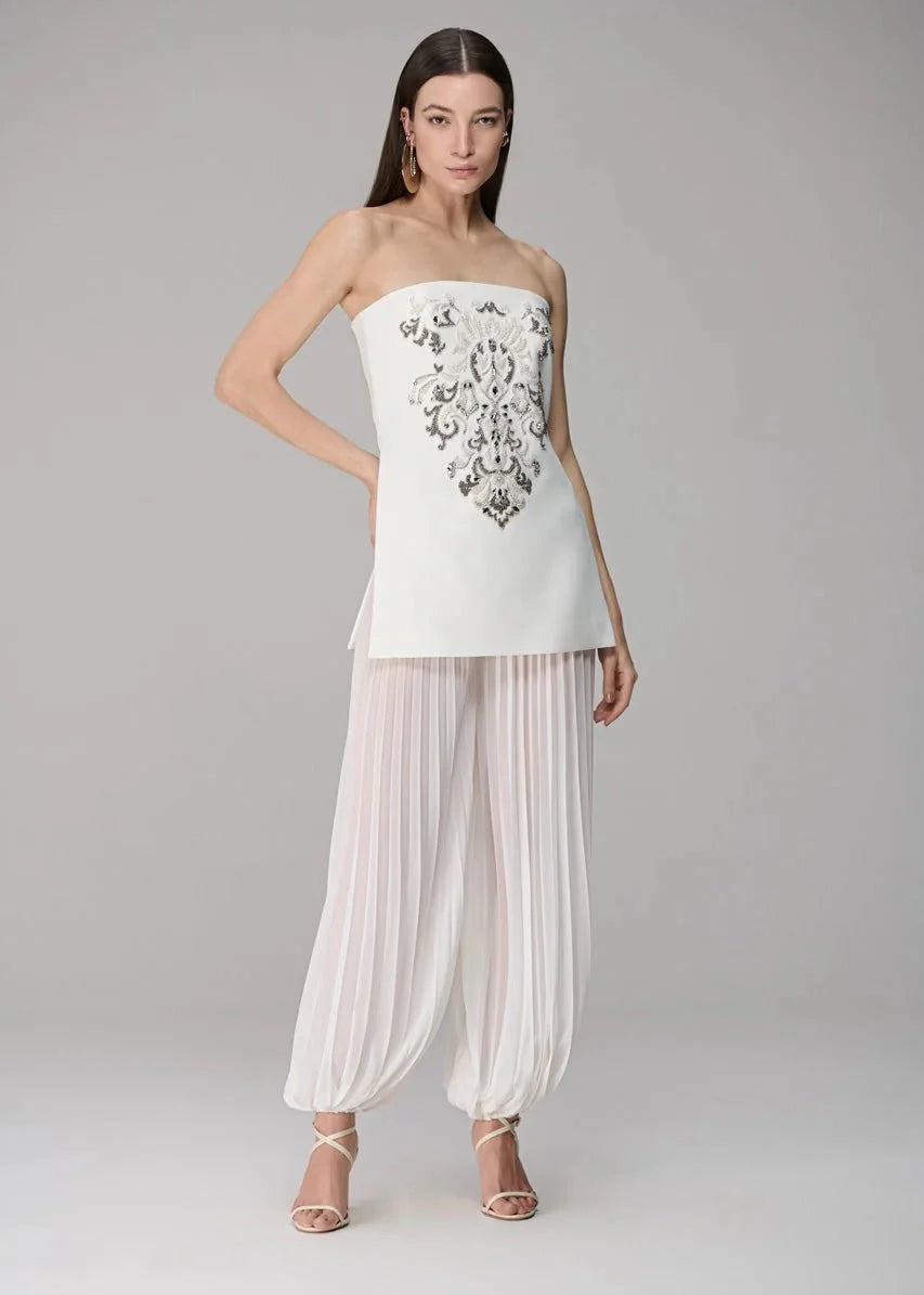 Woman wearing a strapless top with floral embroidery and sheer pants on a gray background