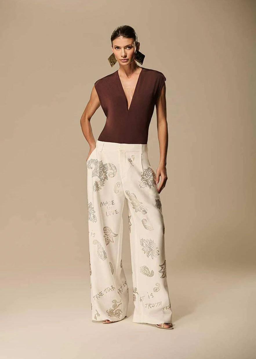 Woman wearing a deep neckline top and wide-leg pants with floral embroidery on a beige background