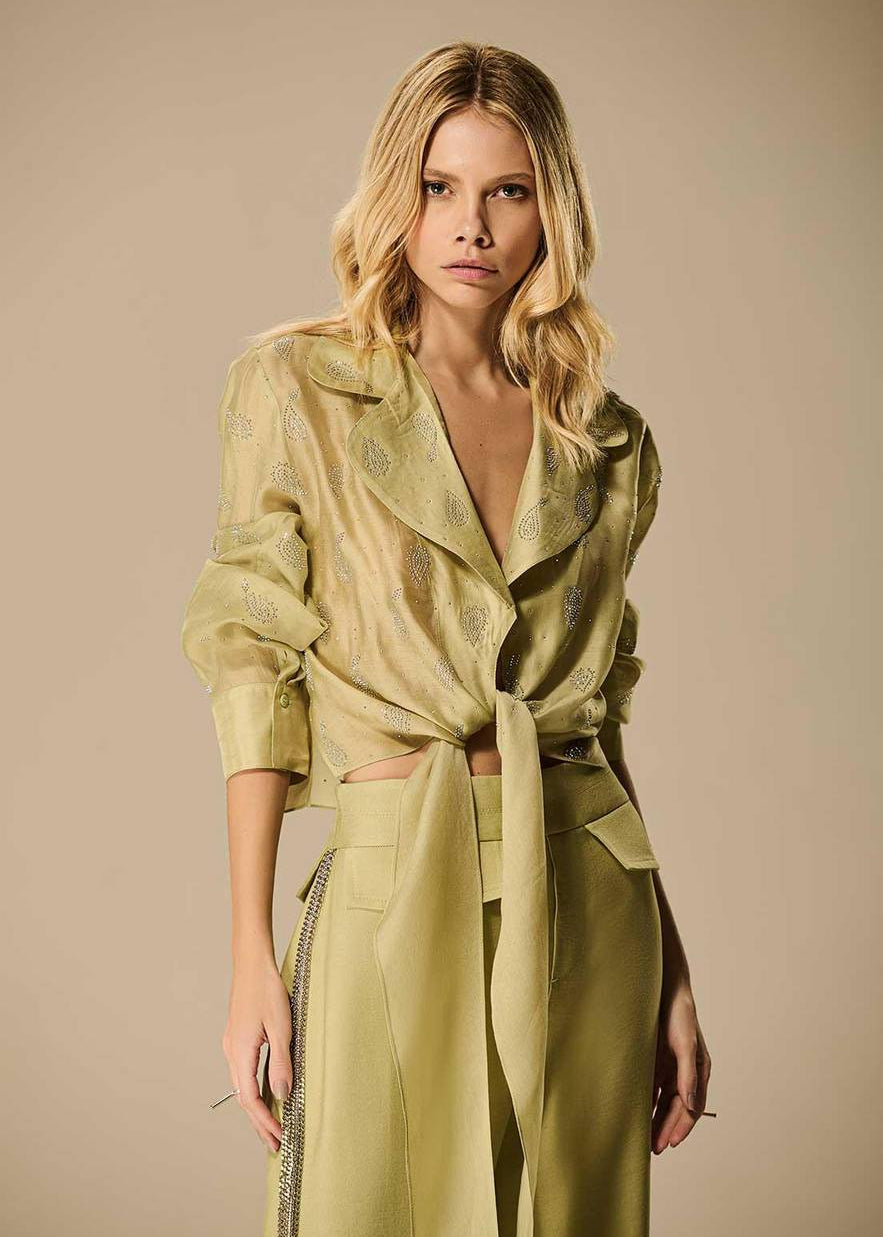 Woman wearing a green outfit with a belt against a beige background