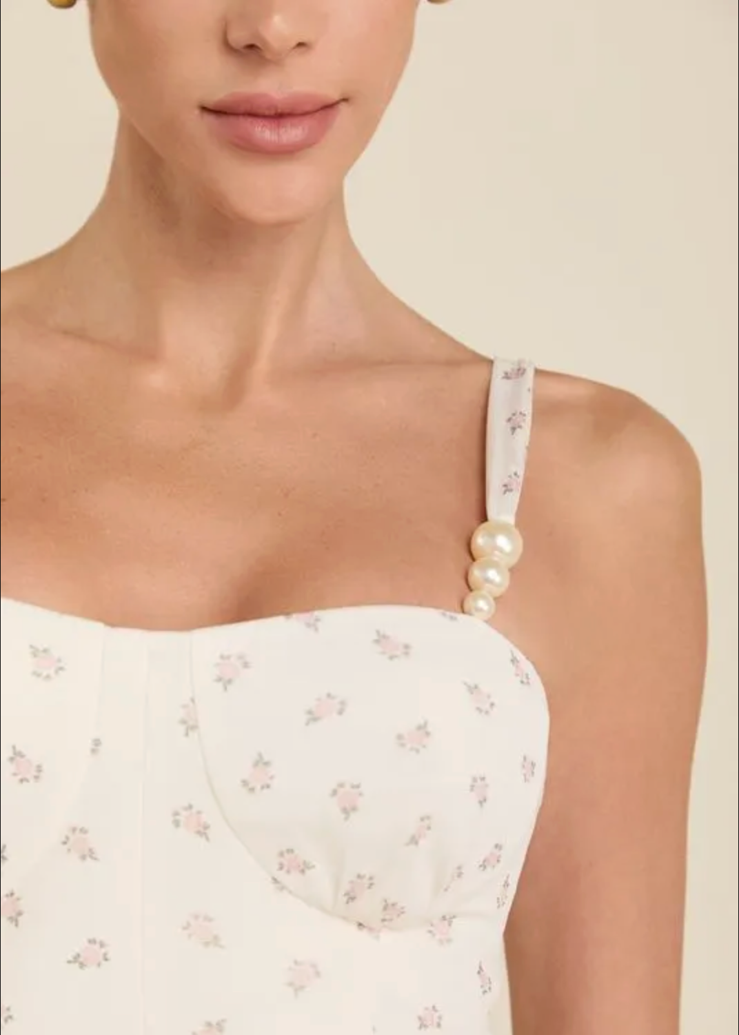 Close-up of a model wearing a white floral strap top with pearl embellishments on the shoulder strap, against a warm beige background.