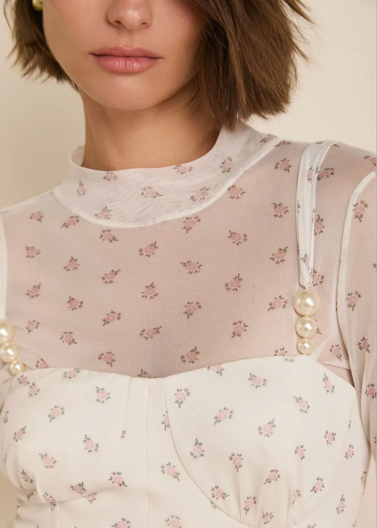 Close-up of a model wearing a sheer blush pink floral mesh mock neck top layered over a white floral corset dress with pearl embellishments.