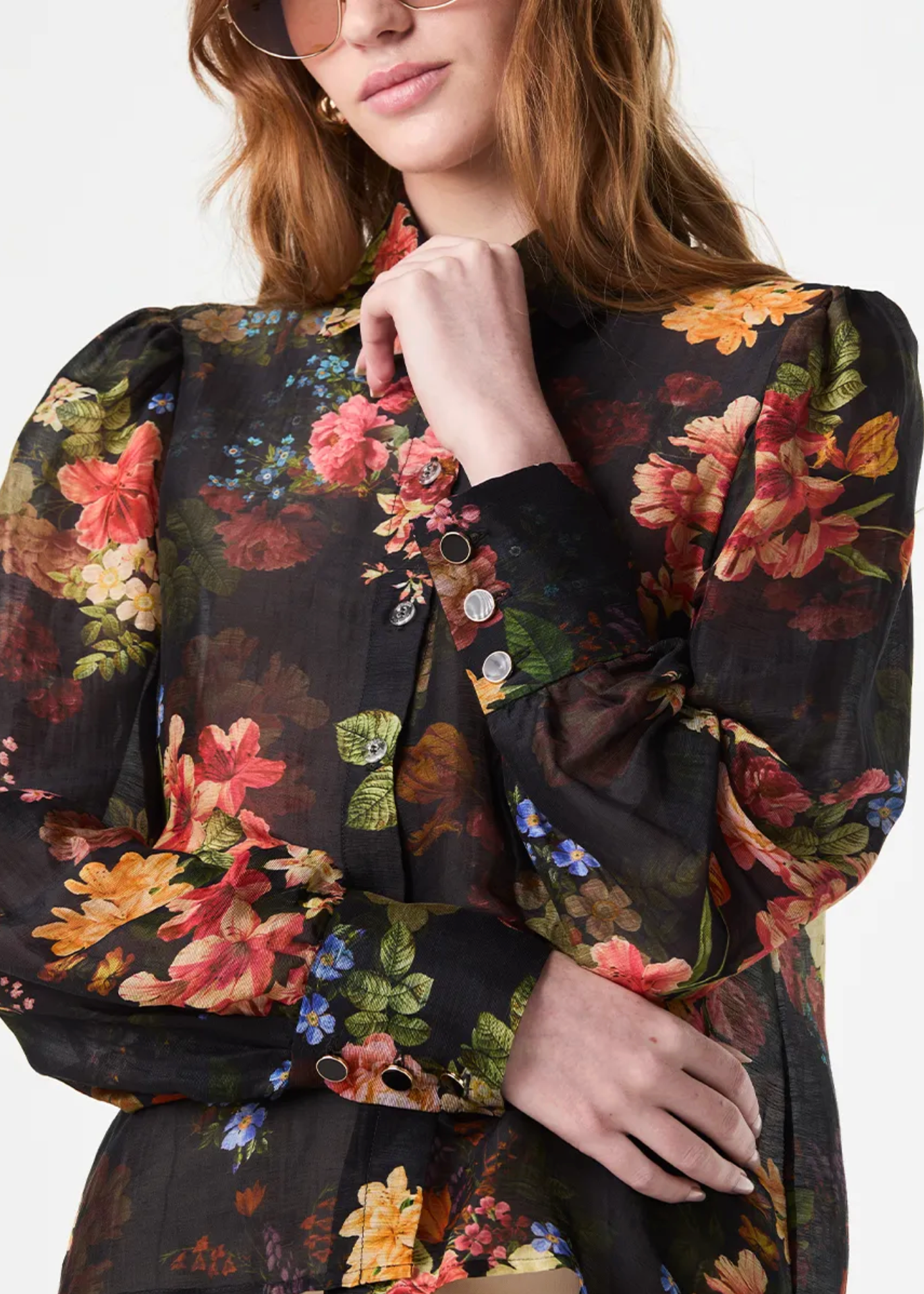 A close-up of a model wearing a black long-sleeve blouse with a vibrant multicolor floral print, featuring puff sleeves and decorative buttons on the cuffs.